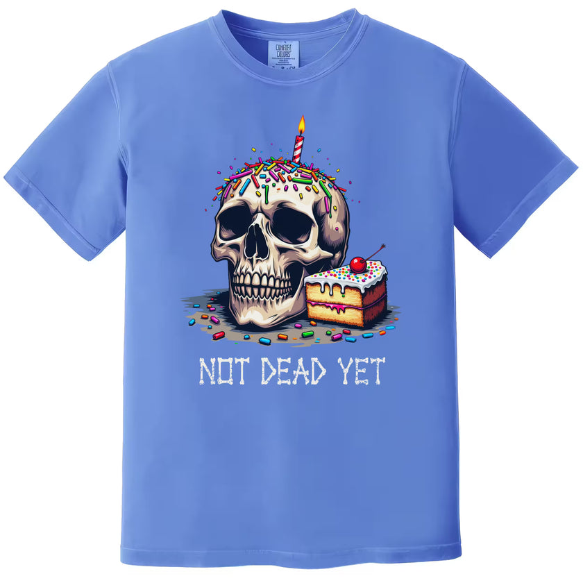 Blue “Not Dead Yet” t-shirt flat lay featuring birthday skull with candle, sprinkles, and cake slice, playful sarcastic graphic tee