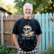 Model wearing black “Not Dead Yet” t-shirt in casual lifestyle setting, showing skull with lit birthday candle, rainbow sprinkles, and cake slice, sarcastic birthday vibe