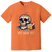 Orange “Not Dead Yet” t-shirt flat lay with skull, birthday candle, sprinkles, and cake slice, playful and sarcastic birthday graphic