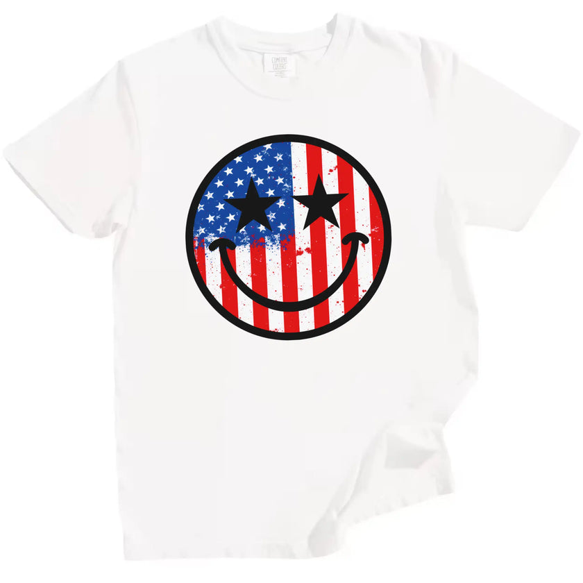 July 4th smiling face graphic tee in white, paint splatter American flag design with star eyes, casual patriotic shirt.