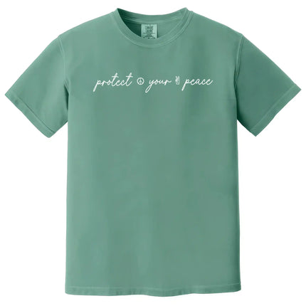 Green “Protect Your Peace” t-shirt flat lay with subtle peace icon details and elegant script font for a simple, mindful design
