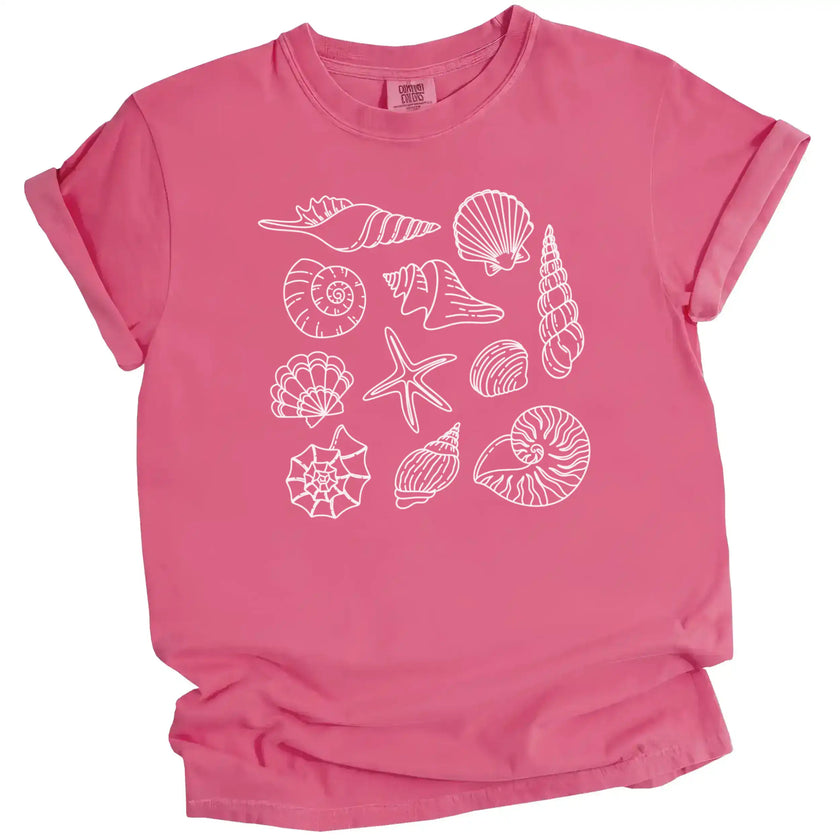 Seashell summer t-shirt in pink, featuring detailed ocean shell varieties arranged in a soft feminine coastal aesthetic layout.