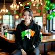 Female model wearing black Buffalo Irish flag buffalo hoodie sitting inside an Irish pub, celebrating St. Patrick’s Day in style