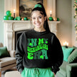 Female model wearing black “In My Shenanigans Era” sweatshirt at home in her living room, cozy and celebrating St. Patrick’s Day