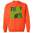 Orange “In My Shenanigans Era” St. Patrick’s Day sweatshirt flat lay showcasing whimsical font and shamrock accents for fun March style