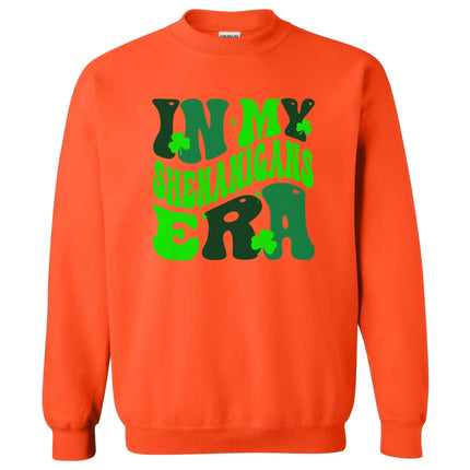 Orange “In My Shenanigans Era” St. Patrick’s Day sweatshirt flat lay showcasing whimsical font and shamrock accents for fun March style