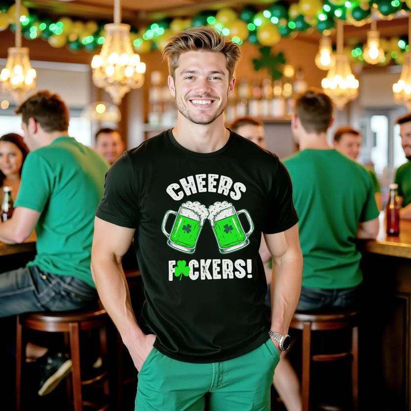Male model wearing black “Cheers Fuckers!” St. Patrick’s Day t-shirt standing at a pub celebrating the holiday