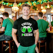 Male model wearing black “Cheers Fuckers!” St. Patrick’s Day t-shirt standing at a pub celebrating the holiday