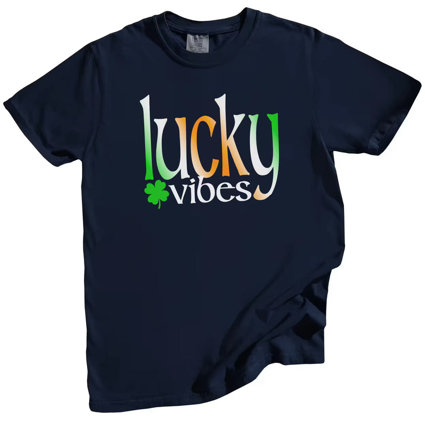 Navy St. Patrick’s Day Lucky Vibes t-shirt flat lay with bold green, white, and orange gradient letters accented by a cheerful four-leaf clover