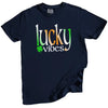 Navy St. Patrick’s Day Lucky Vibes t-shirt flat lay with bold green, white, and orange gradient letters accented by a cheerful four-leaf clover