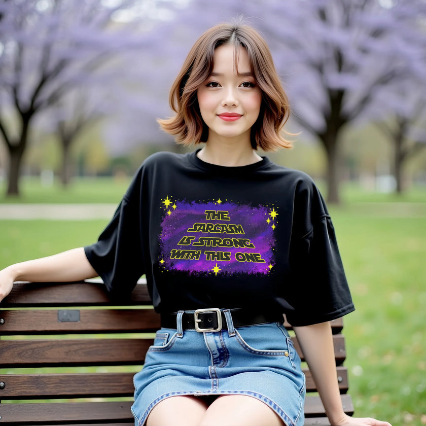 Female model wearing black sarcastic galaxy t-shirt outdoors, ‘The Sarcasm Is Strong With This One’ text with purple blue space design and stars.