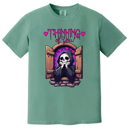 Cute dark humor tee in green, grim reaper in castle window with hearts and ‘Thinking of You’ text, quirky romantic design