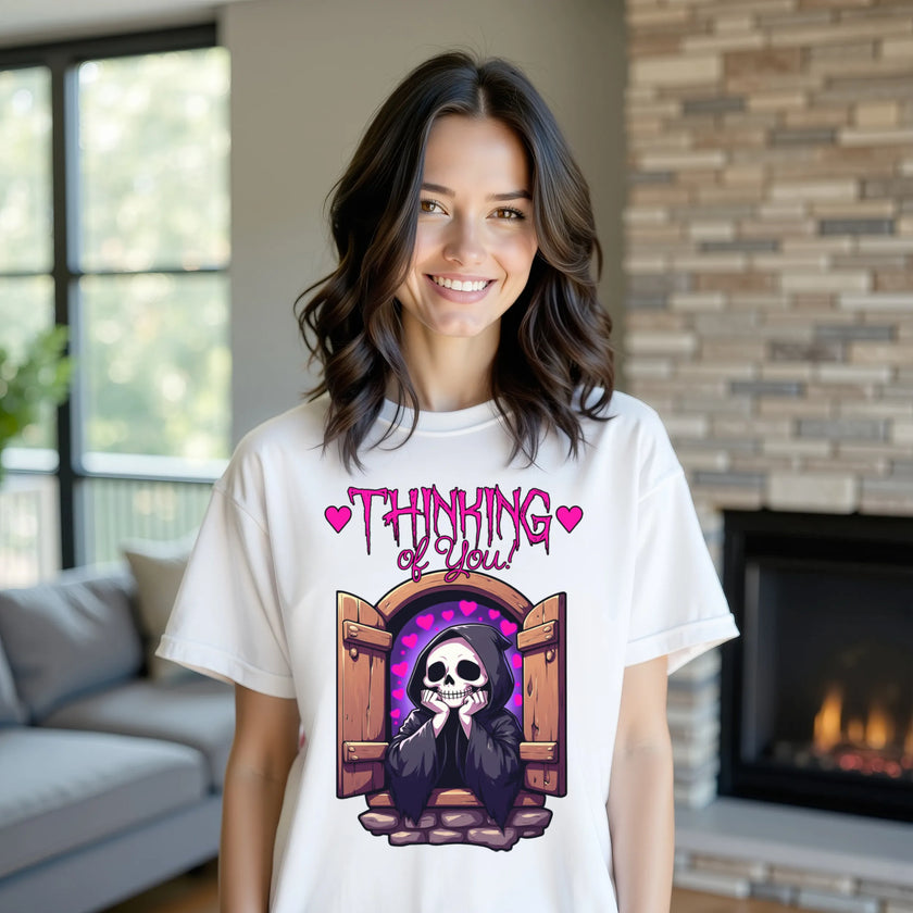 Female model wearing white ‘Thinking of You’ grim reaper t-shirt outdoors, castle window and hearts design, cute dark humor aesthetic outfit.