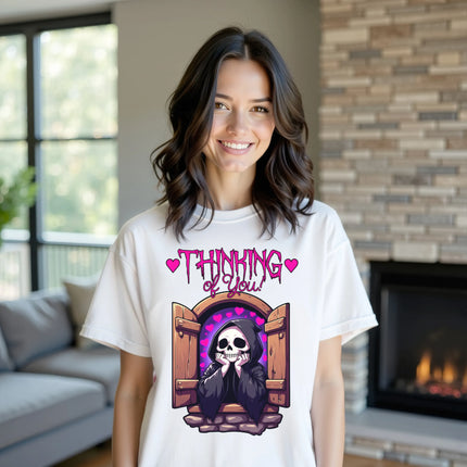Female model wearing white ‘Thinking of You’ grim reaper t-shirt outdoors, castle window and hearts design, cute dark humor aesthetic outfit.