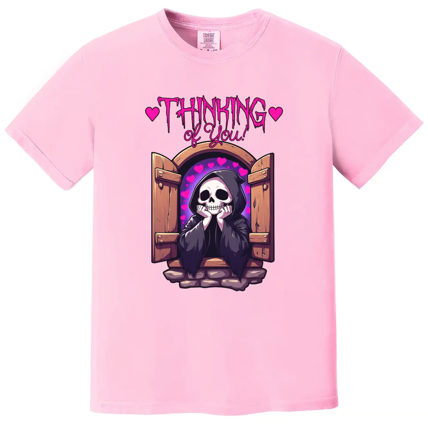Cute grim reaper graphic tee in pink, castle window scene with hearts and ‘Thinking of You’ text, soft dark humor shirt.