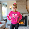 Female model wearing hot pink “Teaching Sweethearts” sweatshirt, standing in her living room, cozy Valentine’s style