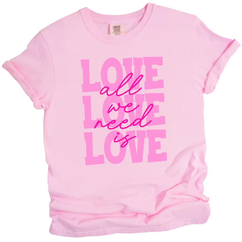 Soft pink ‘All We Need Is Love’ tee with hot pink script, flat lay showcasing feminine Valentine’s style