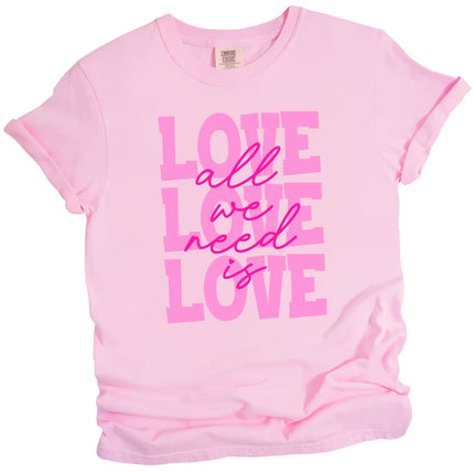 Soft pink ‘All We Need Is Love’ tee with hot pink script, flat lay showcasing feminine Valentine’s style