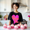 Female model wearing black More Amor Por Favor Valentine’s tee standing in the kitchen, showing playful, romantic style.