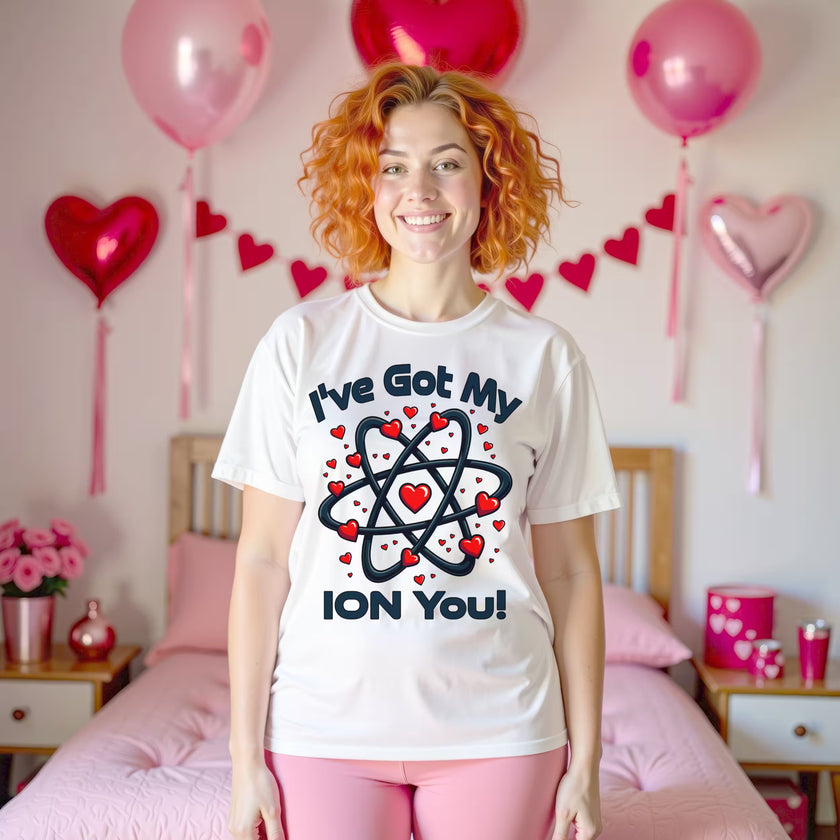 Female model wearing a white “I’ve Got My Ion You” chemistry Valentine shirt standing in a Valentine’s-themed bedroom with festive décor.