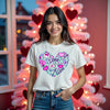 Female model wearing white Valentine’s Love Doodle Tee in living room, styled in front of a pink Valentine’s tree, showing festive romantic vibes.
