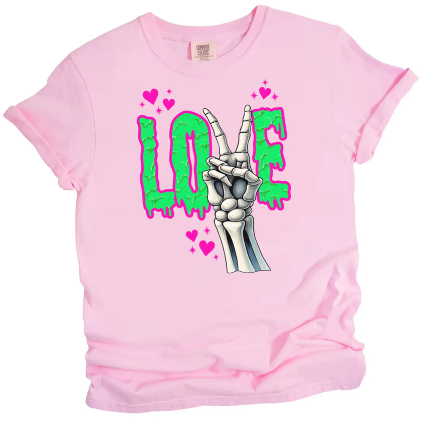 Valentine’s Gothic LOVE t-shirt flat lay in pink with edgy skeleton hand peace sign and green dripping letters.