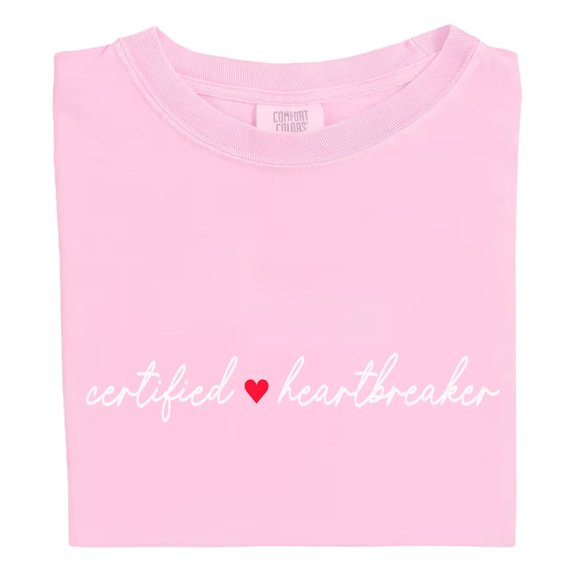 Pink Certified Heartbreaker tee with red heart flat laid on white background.