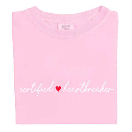 Pink Certified Heartbreaker tee with red heart flat laid on white background.