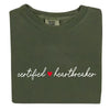 Folded flat lay of green Certified Heartbreaker tee with red heart graphic on white background.