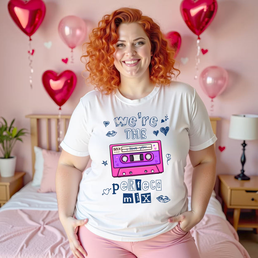 Female model wearing white “We’re the Perfect Mix” Valentine’s tee with pink cassette tape in festive bedroom