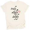 Cream Truly Madly Deeply t-shirt flat lay on white background with bold black lettering and red heart, romantic graphic tee for Valentine’s Day.