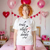 Woman wearing white Truly Madly Deeply t-shirt in Valentine’s-themed bedroom, cozy romantic graphic tee perfect for love-filled moments.