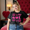 Female model wearing black cowgirl coquette Valentine’s tee standing in a fancy hotel room decorated for Valentine’s Day.