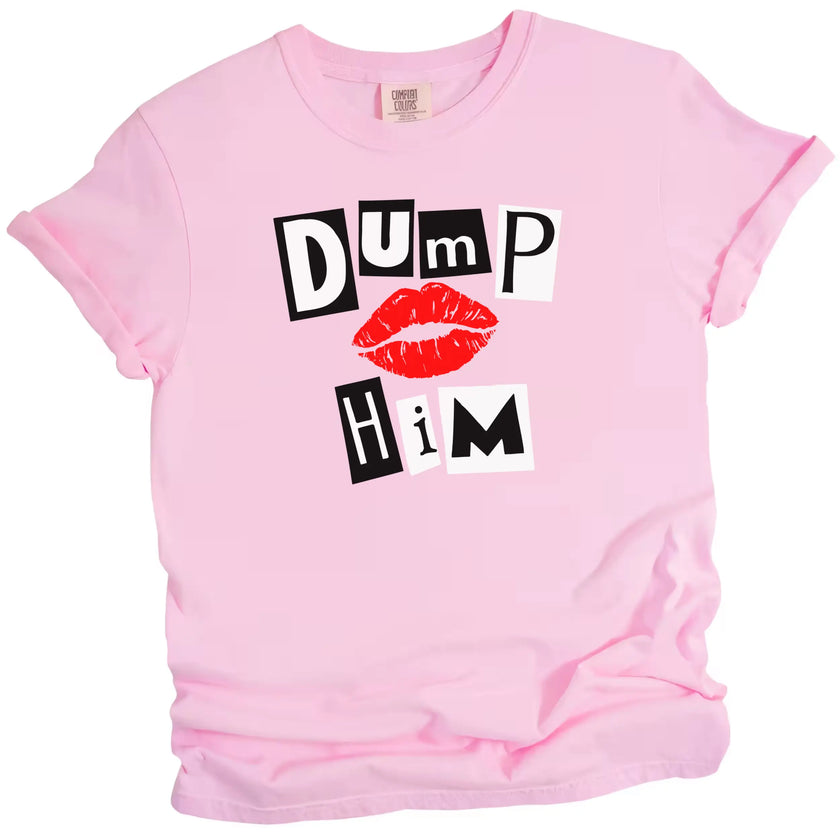Light pink “Dump Him” tee flat lay on white background, bold black and white letters with red lips graphic.