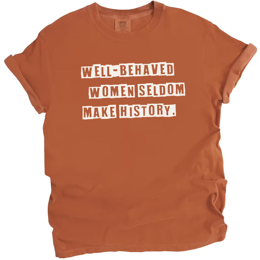 Orange “Well-Behaved Women Seldom Make History” t-shirt flat lay highlighting empowering feminist message with clean typography