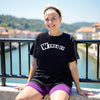 Female model wearing black “Woman Up” t-shirt sitting casually, showing confident and empowering girls-supporting-girls energy